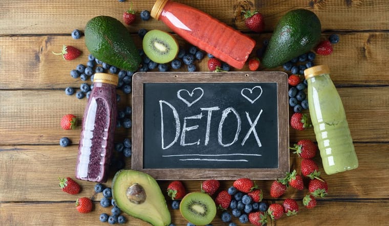 Juices, fruit, and sign reading "detox" over a wooden background.