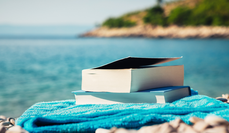 Books on a towel in front of a lake.