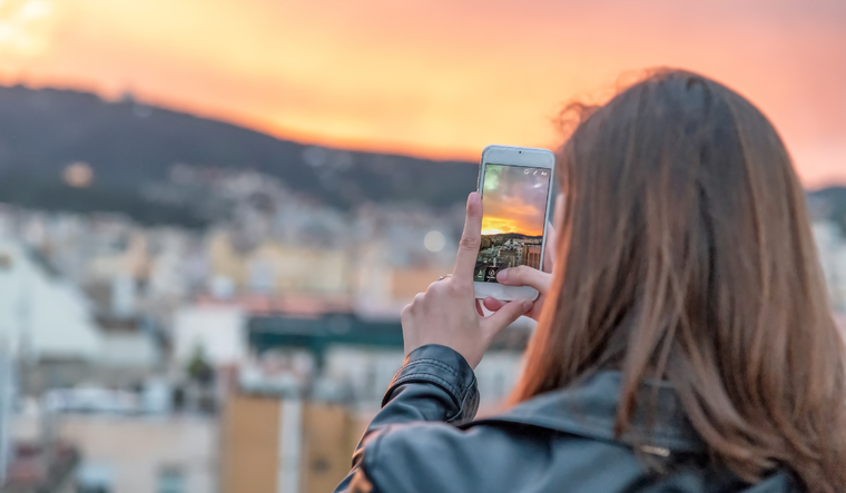 A woman takes a picture of a sunset.